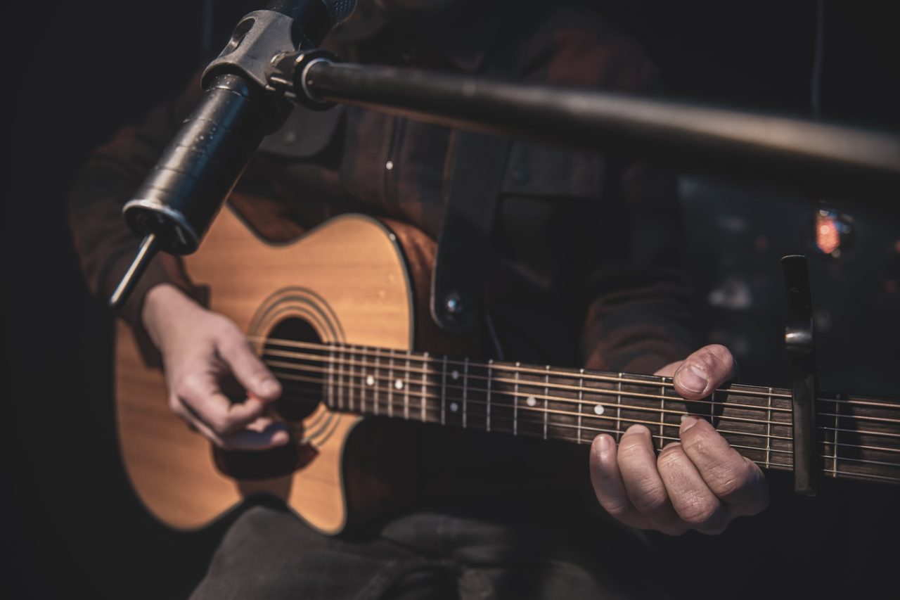 Close up a man plays an acoustic guitar in a dark room.