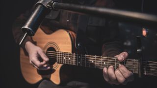 The guitarist plays an acoustic guitar with a capo in front of a microphone. The concept of music recording, rehearsal or live performance.